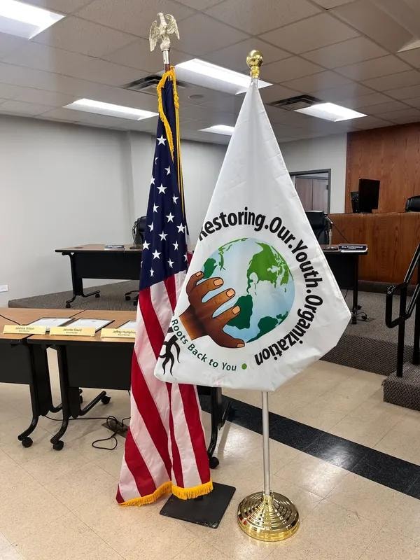 American flag and Restoring Our Youth Organization flag displayed at an official board meeting